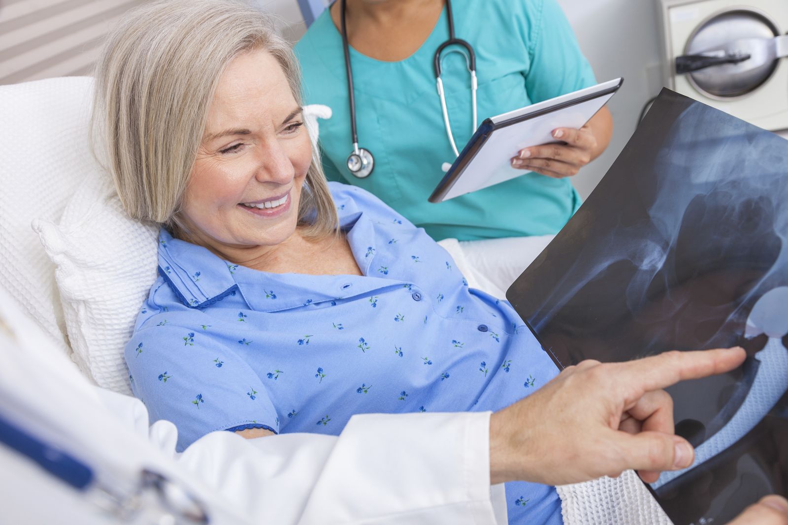 A nurse shows a patient in bed her X-ray on a tablet